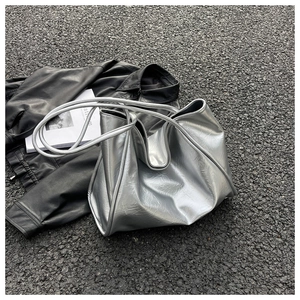 Détail du grand sac cabas argenté avec texture plissée sur fond de bitume urbain
