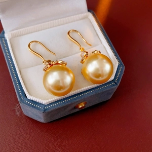 Boucles d'oreilles perles dorées avec zircon dans une boîte à bijoux en velours bleu