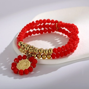 Macro view of red faceted beads and gold St. Benedict medal on a layered bracelet