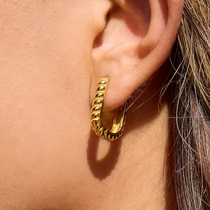 Close-up of gold U-shaped twisted stainless steel hoop earring worn on a model's ear