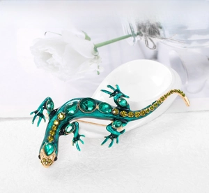 Vue macro d'une broche lézard en émail vert avec cristaux sur support en porcelaine