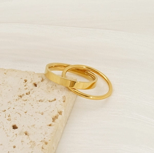 Detailed close-up of two minimalist gold spinning rings on a white textured background