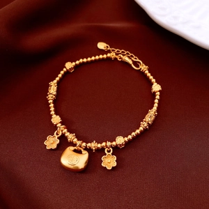 Macro shot of 24K gold plated beaded bracelet with floral charms and Fu lock on velvet