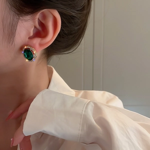 Dettaglio di orecchini a perno verde smeraldo con strass bianchi indossati dal modello