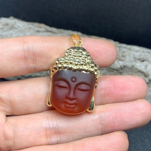 Macro shot of Buddha pendant made of red carnelian and gold metal held by hand