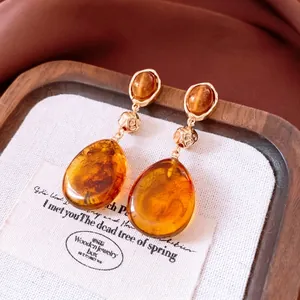 Retro amber resin waterdrop pendant earrings with gold accents on a luxury display tray