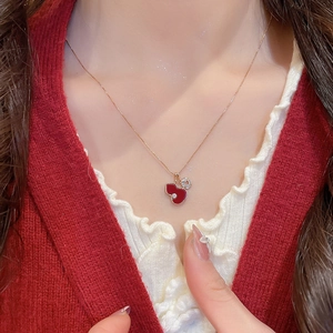 Macro shot of red enamel gourd pendant with small coin charm on a golden chain
