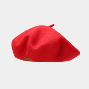 Detail of red wool beret showing the thick felt texture and brown leather logo tag