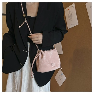 Detail of pink suede bucket bag showing chain strap and metallic ball charm on model