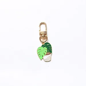 Close-up of golden keychain featuring a green monstera plant enamel pendant detail