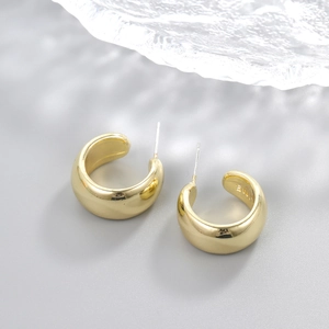 Close-up of golden teardrop earrings with S925 hallmark on polished metal surface