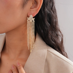 Detail of gold-tone long fringe earrings with rhinestones worn by a model in a suit