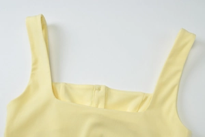 Detail view of square neckline and shoulder straps on a light yellow knit vest