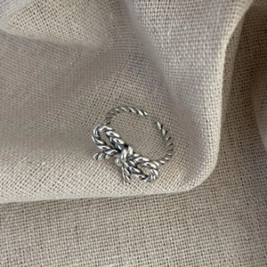 Macro detail of 925 sterling silver twisted rope bow ring on beige textured linen fabric