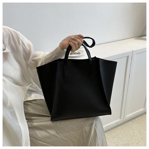 Detail of a large black PU leather tote bag held by a model in a minimalist setting