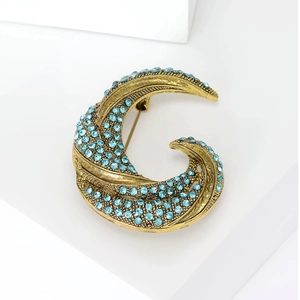 Vintage crescent moon gold brooch with blue rhinestones on a white geometric stand