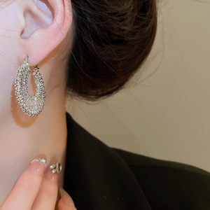 Detail of silver woven hoop earring featuring intricate braided metal texture on model