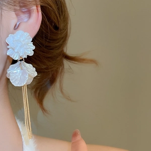 Detail of white acrylic flower tassel earrings worn on ear with gold chain accents