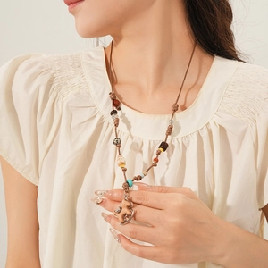 Dettaglio collana boho con pendente in legno e perline su un top bianco strutturato