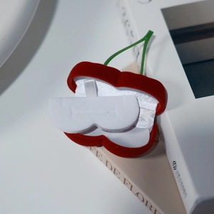Primer plano de un joyero de terciopelo con forma de cereza roja y forro interior blanco