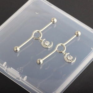 Detail of silver industrial barbell earring featuring dangling pavé moon and star charms