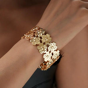 Detail of a wide gold metal bracelet featuring an intricate hollow floral pattern