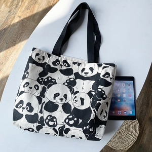 Detail of panda print canvas tote bag with black strap next to a tablet for scale