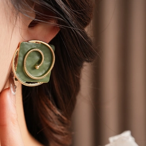 Close-up of vintage dark green square earrings with golden spiral pattern on a model