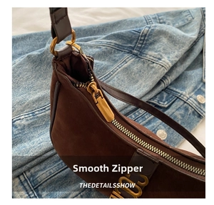 Detailed close-up of smooth gold zipper and suede texture on brown shoulder bag