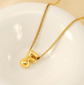 Close-up of a golden bubble-style letter F pendant on a delicate chain in a white tray