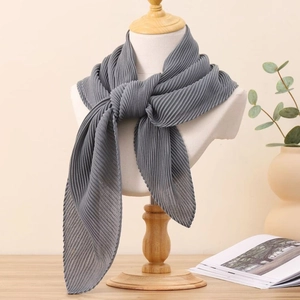 Détail d'un foulard plissé gris noué sur un mannequin dans un décor chaleureux