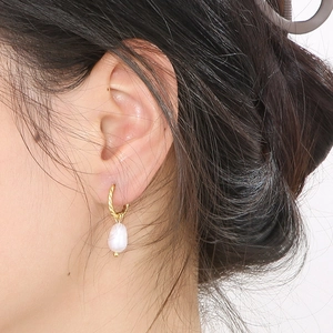 Detailed close-up of golden twisted hoop earrings with irregular baroque pearl drop
