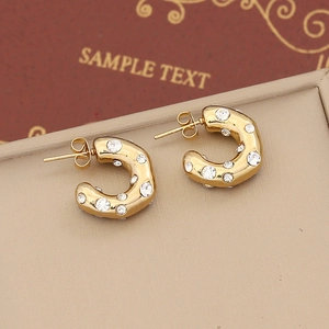 Detailed close-up of C-shaped golden earrings with sparkling rhinestones and studs