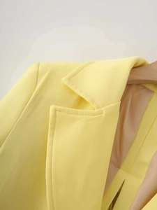 Detail of bright yellow satin blazer featuring notched lapels and fine stitching quality