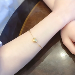 Detailansicht eines goldenen Herzanhänger-Armbands mit Perlen auf einer Metallkette