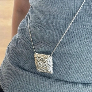 Détail macro d'un pendentif carré argenté avec texture tissée sur chaîne serpent