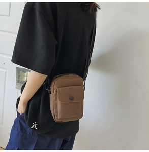 Detailed side view of a brown canvas crossbody bag with adjustable strap and front pocket