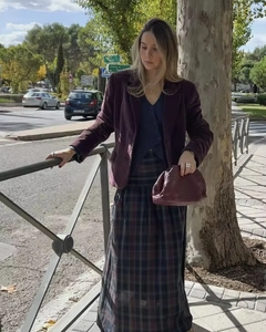 Dettaglio blazer in velluto rosso abbinato a gonna scozzese scura e pochette in pelle a pieghe