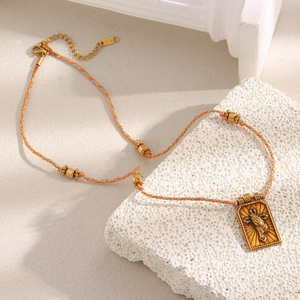 Detail of woven orange and blue cord necklace with 18K gold plated tarot cross pendant