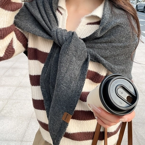 Détail d'un châle en maille gris foncé avec étiquette en cuir sur un pull à rayures fines