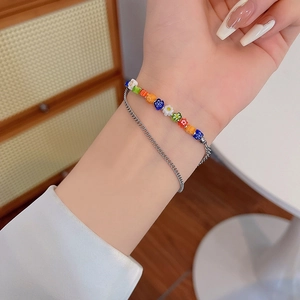 Dettaglio di un bracciale a due strati con perle floreali colorate e catena in metallo