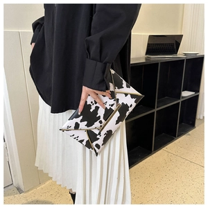Close-up of cow print clutch bag with gold metal trim held by a fashion model