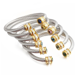 Close-up of twisted stainless steel cable bracelets with colorful gemstone ends in 18k gold