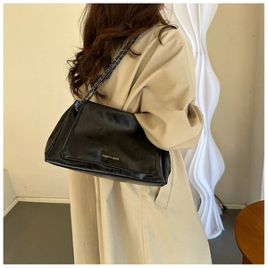 Close-up of black leather underarm bag with metal chain strap on minimalist beige coat