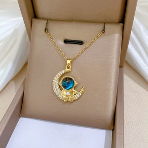 Macro detail of gold-tone astronaut moon pendant necklace with pavé crystal settings