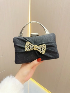 Close-up of black glitter evening clutch featuring a golden rhinestone bow and metal handle