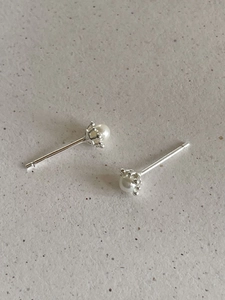 Detailed close-up of pearl stud earrings featuring a silver crown-shaped setting