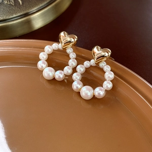 Close-up of heart-shaped gold stud with elegant white pearl hoop on ceramic plate
