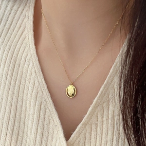 Close-up of a minimalist gold oval pendant necklace worn over a soft beige sweater