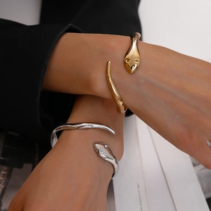 Macro shot of minimalist gold and silver snake open bracelets with polished metal texture